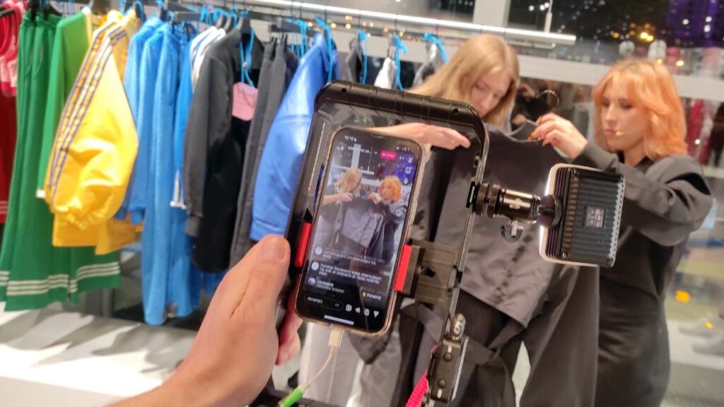 Transmisja na Instagram ze sklepu, smartfon w uchwycie, 2 osoby pokazujące produkty